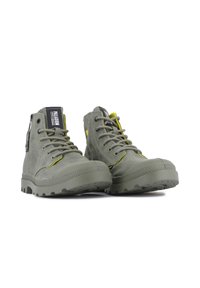 Grüne Canvas-Ankle-Boots mit Gummisohle und gelben Akzenten an den Ösen. Schnürsenkel und ein Logotag sind an der Seite sichtbar.