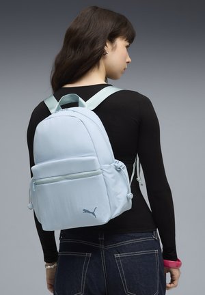 Uno zaino azzurro chiaro di forma arrotondata, con una tasca frontale con cerniera, due tasche laterali e spallacci regolabili. Logo visibile.