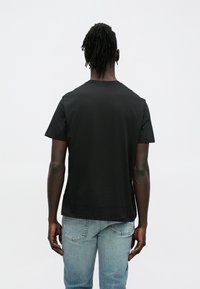 Czarny bawełniany t-shirt z krótkim rękawem, o kroju z okrągłym dekoltem i luźnym fasonie, zestawiony z jasnoniebieskimi dżinsami.