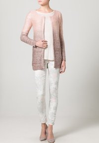 Lätt cardigan i gradient rosa och brunt, glittrig struktur, öppen framsida, matchad med en ljus topp och byxor med blommönster.