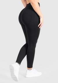 Leggings neri a vita alta con una texture liscia, design aderente e look senza cuciture, abbinati a scarpe atletiche bianche e calzini alla caviglia con motivo.