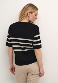Sort strikket sweater med vandrette cremefarvede striber, korte ærmer og en rund halsudskæring, vist fra ryggen mod en neutral baggrund.