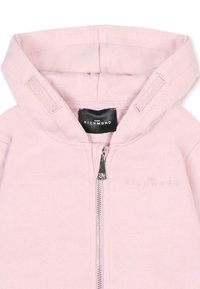 Sweat-shirt rose clair avec un zip sur le devant, capuche ajustable et tissu texturé. Présente une étiquette de logo et un nom de marque en relief sur le devant.