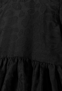 Robe noire avec un motif léopard texturé, présentant un ourlet à volants et un tissu lisse. Le design est minimaliste et monochrome.
