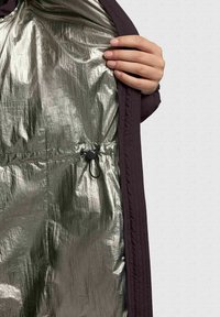 A purple jacket is shown opened, revealing a shiny, metallic silver interior with a pullcord adjustment feature at the waist.