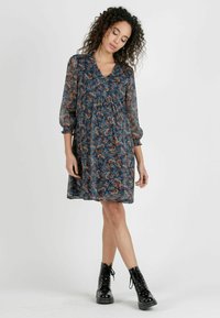 Blå blommig chiffongklänning med en volangkrage och puffärmar, med en löst sittande och knälång design. Accentuerad med svarta snörboots.
