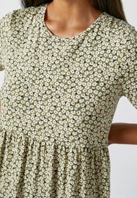 Robe florale en tissu doux et léger ; fond vert avec de petites fleurs blanches et des accents rouges ; manches courtes et taille froncée.