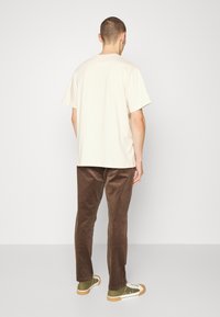 Beige katoenen t-shirt gecombineerd met bruine corduroy broek. De outfit heeft een losse pasvorm, korte mouwen en groene sneakers met witte zolen.