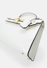 Biała torebka z tłoczonym wzorem krokodyla, czarnymi wykończeniami, złotymi elementami metalowymi i ozdobną klamrą. Charakteryzuje się wyraźną, usztywnioną formą oraz gładką teksturą.