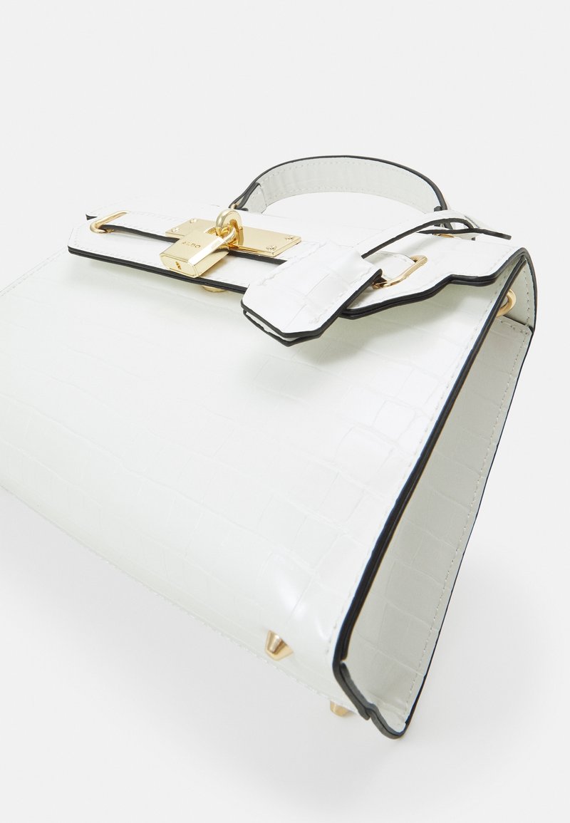 Biała torebka z tłoczonym wzorem krokodyla, czarnymi wykończeniami, złotymi elementami metalowymi i ozdobną klamrą. Charakteryzuje się wyraźną, usztywnioną formą oraz gładką teksturą.