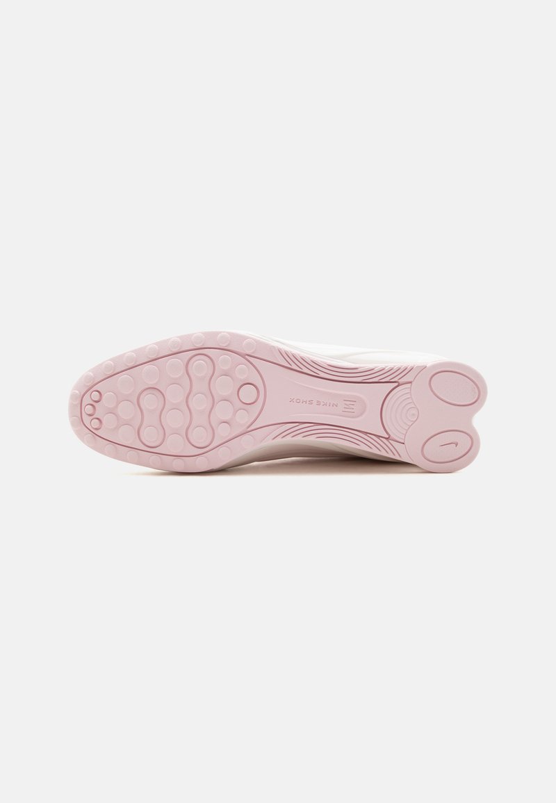 Suela de un zapato blanco de Nike con tacos de goma rosa que presentan patrones circulares y el logo de Nike cerca del talón.