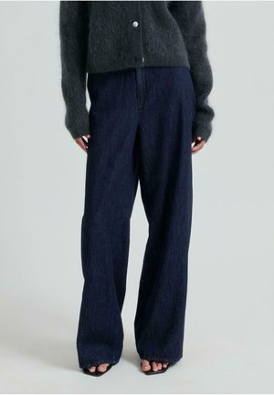 Wijduitlopende donkere denim jeans met een hoge taille, voorzien van een gladde textuur en subtiele stikdetails. Gepaard met een donkere fuzzy trui.