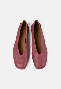 Zapatos de piel marrón con diseño tipo slip-on, punta redondeada, suela plana y costuras mínimas. El interior presenta una plantilla en tono beige con el logotipo "CAMPER".