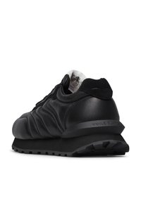 Sneaker in pelle nera con design trapuntato, punta arrotondata e tallone testurizzato. Presenta una suola in gomma a contrasto e branding sul lato.