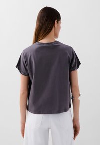 T-shirt gris à manches courtes avec une coupe décontractée, présentant un col rond et des manches retroussées. Tissu lisse avec une texture douce.
