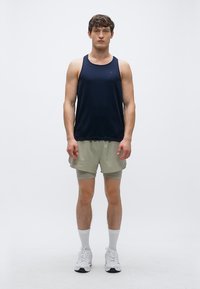 Maiou sportiv bleumarin fără mâneci, asortat cu pantaloni scurți verde deschis, purtat cu adidași albi și șosete albe până la genunchi. Design și croială simple.