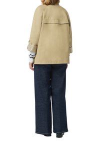 Beżowa kurtka o luźnym kroju, z tylnym karczkiem i podwiniętymi rękawami, zestawiona z ciemnoniebieskimi spodniami dżinsowymi w szerokim kroju. Gładka faktura materiału.