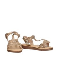 Sandalias beige con múltiples correas cruzadas, acentos metálicos, suela plana y una plantilla texturizada para mayor comodidad.