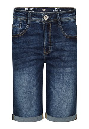 Dreng i beige T-shirt med palmeprint, denimshorts rullet op i kanten, hvide sneakers og hvide sokker med sorte striber, stående.