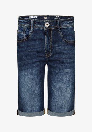Dreng i beige T-shirt med palmeprint, denimshorts rullet op i kanten, hvide sneakers og hvide sokker med sorte striber, stående.