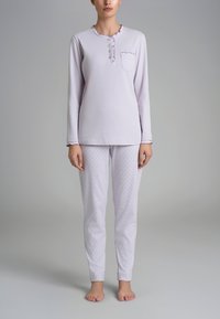 Maglietta da pigiama a maniche lunghe viola chiaro con scollatura a ruffles, tre bottoni e una tasca; abbinata a pantaloni bianchi con piccoli pois rosa.