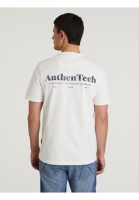 Bijela pamučna majica kratkih rukava s tamnoplavi natpisom "AuthenTech" i dodatnim brendingom na poleđini, u kombinaciji sa svijetloplavim farmerkama.