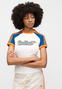 Μπλούζα με μανίκια raglan, λευκό κορμό, μπλε μανίκια και πορτοκαλί λεπτομέρειες. Διαθέτει γραφικό με τη λέξη «New York» σε πορτοκαλί και μπλε. Υλικό από υφασμένο βαμβάκι.