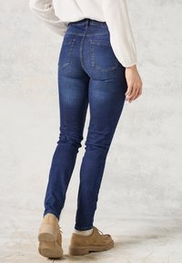 Mörkblå skinny jeans med hög midja, fem fickor och kontrasterande sömmar, tillsammans med ljusbruna snörskor.