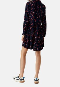 Marineblauwe jurk met een roze abstract patroon, lange mouwen en een gelaagde rok. Gecombineerd met zwart-witte sneakers met blauwe accenten.