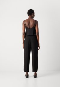 Svart satin-camisole med justerbare stropper, kombinert med høyt liv svart bukse med en skreddersydd passform og baklommer.