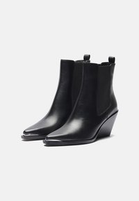 Botas de tobillo de cuero negro con punta afilada, paneles laterales elásticos y un tacón de cuña. Acabado suave con un diseño minimalista.