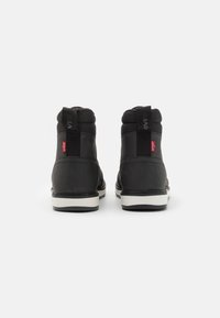 Zapatillas altas negras con parte superior sintética texturizada, cuello acolchado y suelas de goma blanca. Presentan acentos de logo y paneles laterales elásticos.