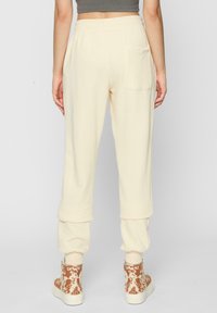 Crèmekleurige sweatpants met een relaxte pasvorm, ribbelboorden en een achterzak, gedragen met patroon high-top sneakers.