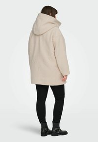 Heledad beež, üleeriline, kapuutsiga mantel, millel on tekstuuriga kangas, pikad varrukad ja sirge äär. Kanda mustade kitsaste pükste ja pahkluuni ulatuvate saapadega.