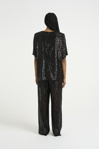 Svart paljettoutfit med en kortärmad topp och löst sittande byxor. Tyget har en glänsande, strukturerad yta som reflekterar ljus.
