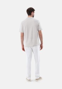 Polo grigio chiaro a maniche corte con colletto classico, texture morbida e taglio dritto, abbinato a pantaloni bianchi aderenti e sneakers beige.