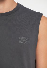 Ärmelloses graues Tanktop aus glattem Stoff mit strukturiertem Stickerei, auf der steht "DISZIPLIN IST KEIN SCHMUTZIGES WORT RON DORFF."