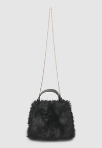 Sac en fausse fourrure noire avec une courte poignée en cuir et une longue chaîne dorée fine sur un fond gris.