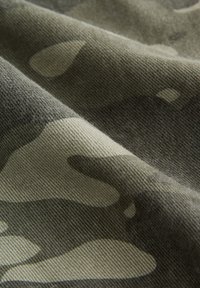 Gros plan sur un tissu camouflage vert et beige avec une surface tissée texturée et des plis doux.