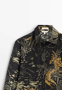 Chemise en soie noire ornée de motifs complexes en or et crème représentant des poissons et des éléments botaniques, avec un col classique et une fermeture à boutons.