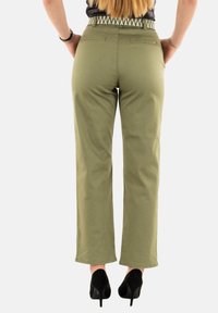 Pantaloni in cotone verde con taglio dritto, caratterizzati da una cintura pattern e due tasche posteriori. Abbinati a tacchi alti neri.