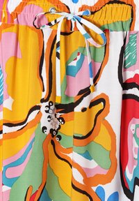 Tissu à motif floral avec des couleurs vives, y compris jaune, rose et vert. Il présente une taille élastique avec un cordon de serrage.
