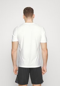 Jersey atlético blanco con mangas cortas, tejido de malla texturizado, patrón sutil y costuras en contraste a lo largo de las mangas y el escote.