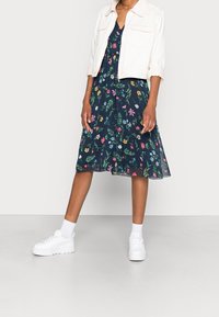 Floral dress with a navy background, featuring multicolored flowers. Paired with a white cropped denim jacket and white platform sneakers.