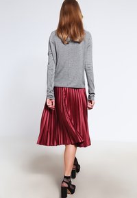 Grå långärmad topp med en slät yta, tillsammans med en plisserad bourgogne kjol som har ett elastiskt midjeband och en flödande silhuett.