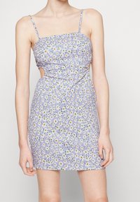 Robe florale lilas à bretelles spaghetti, avec un corsage ajusté, des côtés découpés, et un motif dispersé de marguerites jaunes et blanches.