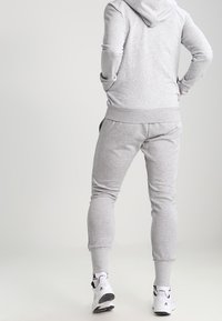 Sudadera con capucha y pantalones de chándal grises hechos de tela suave. Presentan puños acanalados, bolsillos laterales y un diseño ajustado. Se llevan zapatillas deportivas.