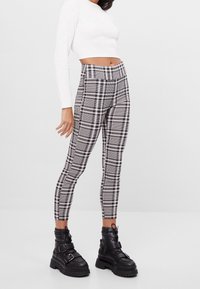 Czarno-białe legginsy w kratkę z wysokim stanem, elastyczny materiał, dopasowany krój, połączone z masywnymi czarnymi botkami za kostkę z akcentami klamrowymi.