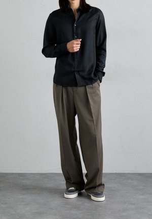 Zwarte button-up shirt met lange mouwen, gecombineerd met losse bruine broeken en grijze sneakers. Soepele stof en een ontspannen pasvorm.