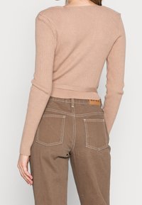 Pull en maille côtelée à manches longues de couleur beige clair associé à un pantalon marron taille haute avec poches arrière et coutures contrastantes.